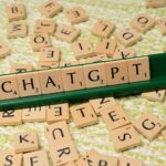 Lettres en bois du jeu Scrabble formant le mot 'CHATGPT' sur un support vert, avec des lettres éparpillées en arrière-plan.