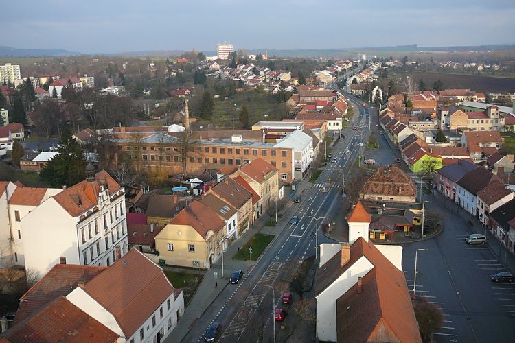 Rousinov : Vue aérienne d'une petite ville européenne avec des maisons aux toits rouges, une rue principale et des espaces verts à l'horizon.