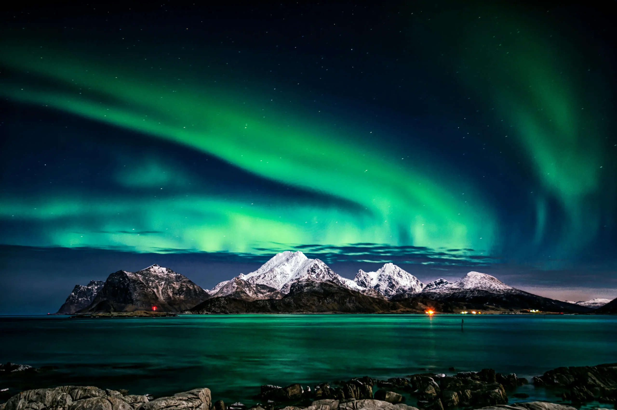 Aurores boréales illuminant un ciel nocturne au-dessus de montagnes enneigées et d'une mer calme en Norvège.