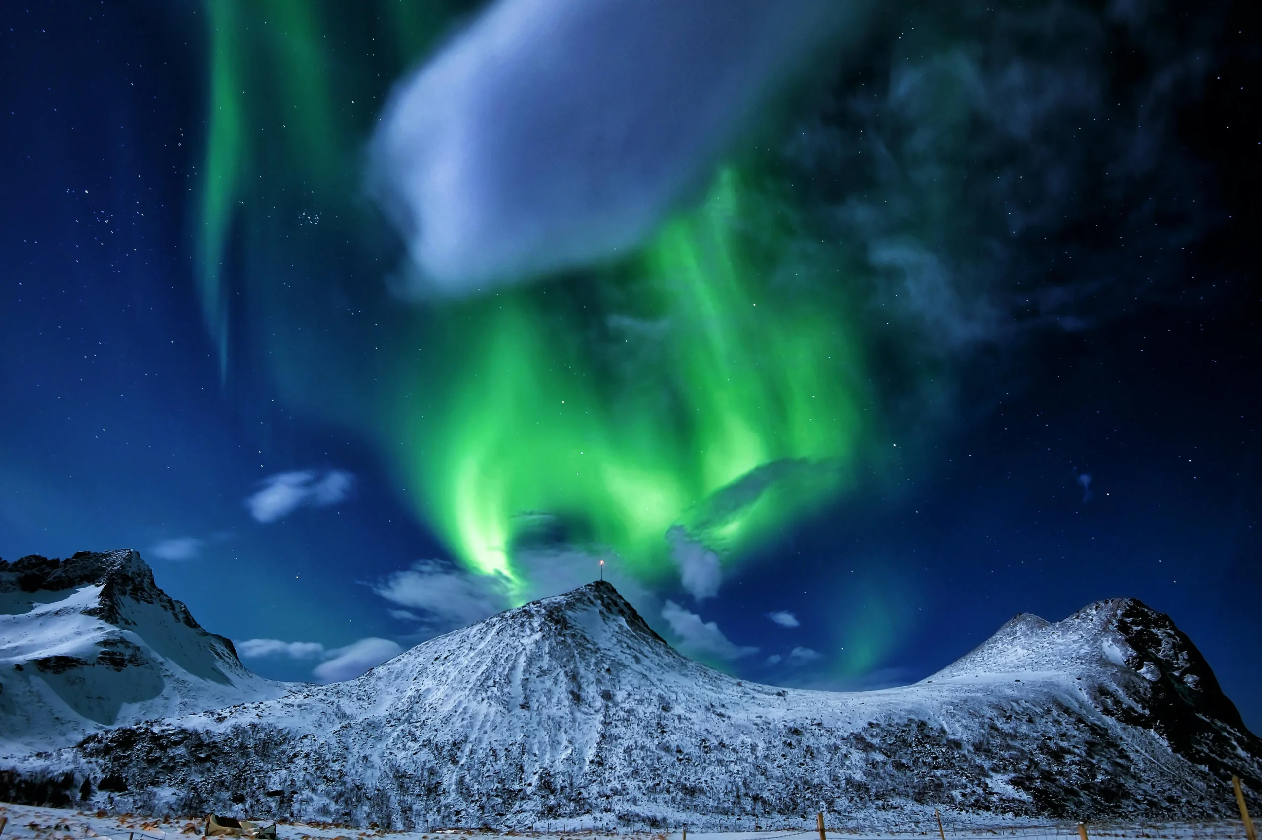 Aurores boréales spectaculaires au-dessus de montagnes enneigées sous un ciel étoilé en Norvège.