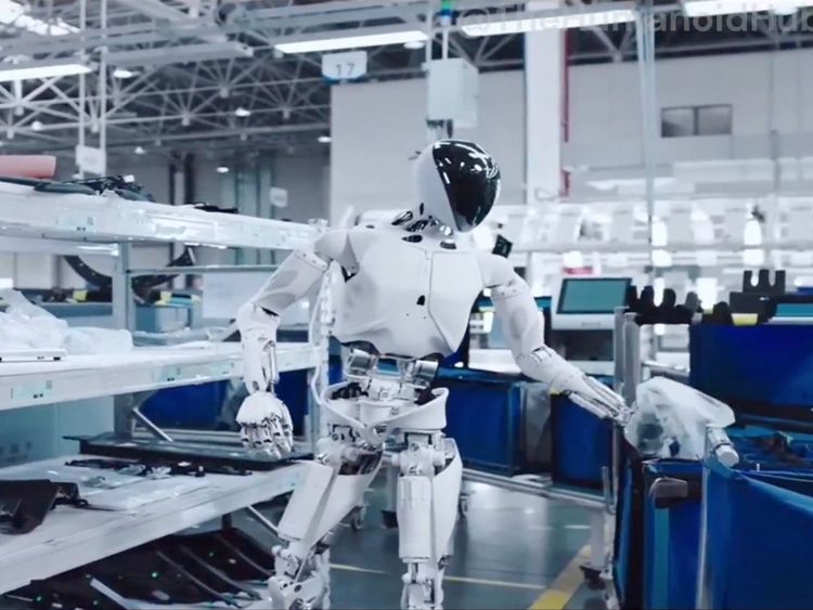 Robot humanoïde blanc travaillant dans un environnement industriel moderne, manipulant des pièces ou du matériel dans une ligne de production.