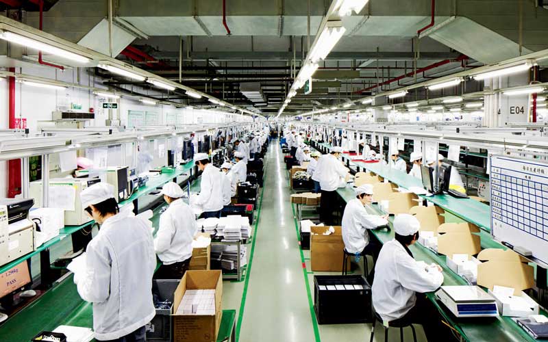 Chaine d'assemblage dans une usine, avec des employés vêtus de blouses blanches et de couvre-chefs, travaillant sur diverses étapes de fabrication.